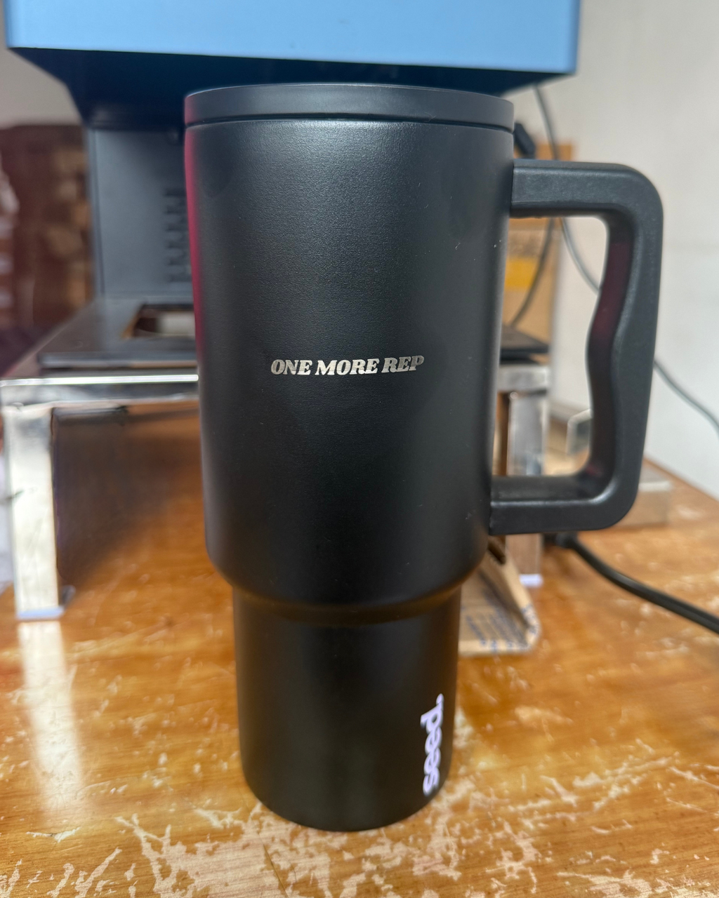 Black travel mug with 'ONE MORE REP' text on a wooden surface stainless steel tumbler 900mL dark knight