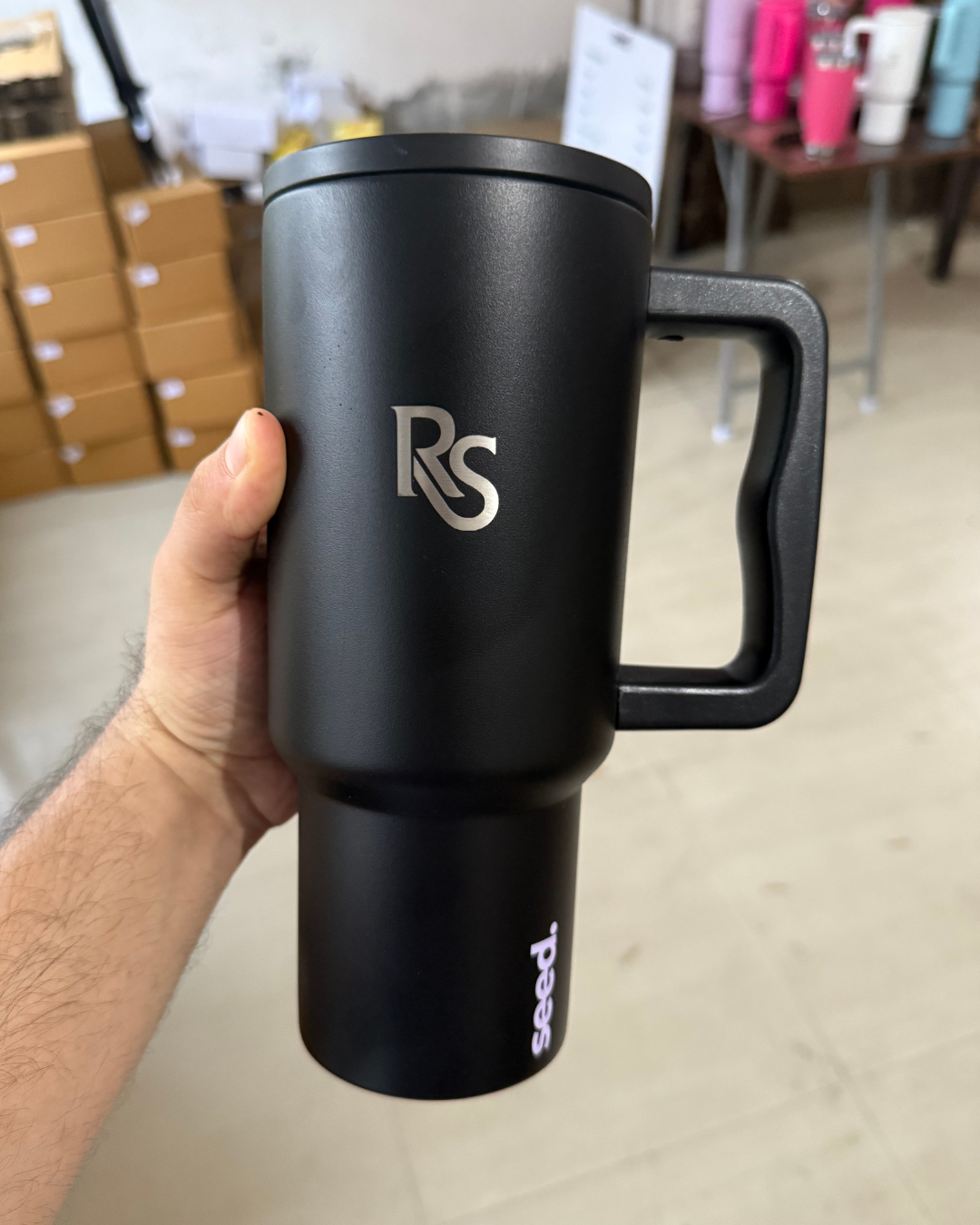 Black insulated stainless steel tumbler 900mL dark knight with a logo held by a hand in an indoor setting.