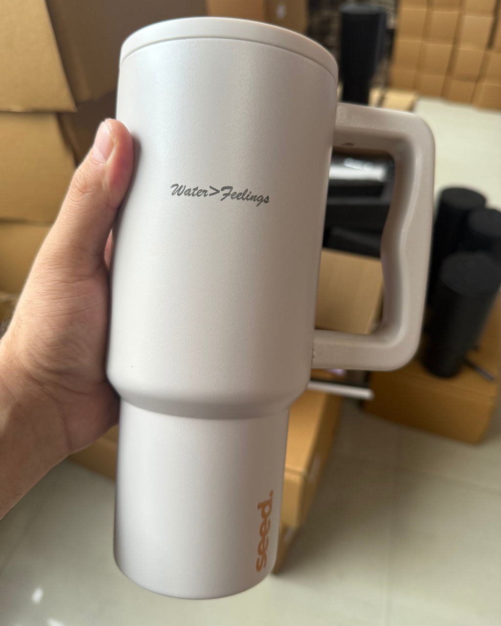 White mug with 'Water > Feelings' text held by a hand, with a blurred indoor background. stainless steel tumbler 900mL milk tea