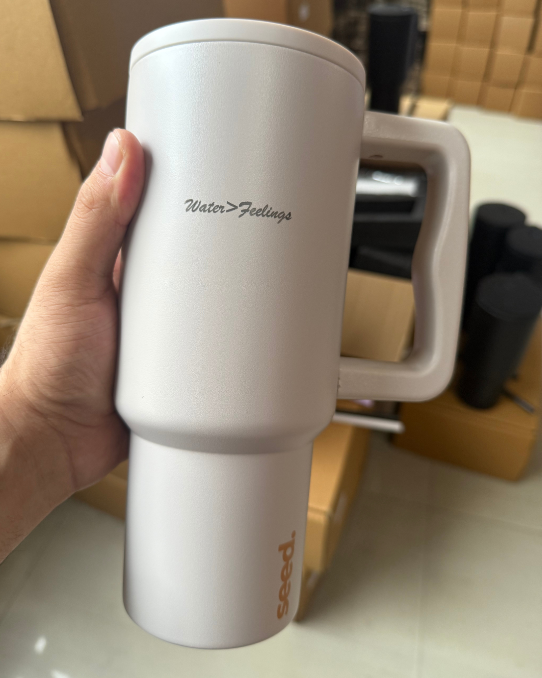 White mug with 'Water > Feelings' text held by a hand, with a blurred indoor background. stainless steel tumbler 900mL milk tea