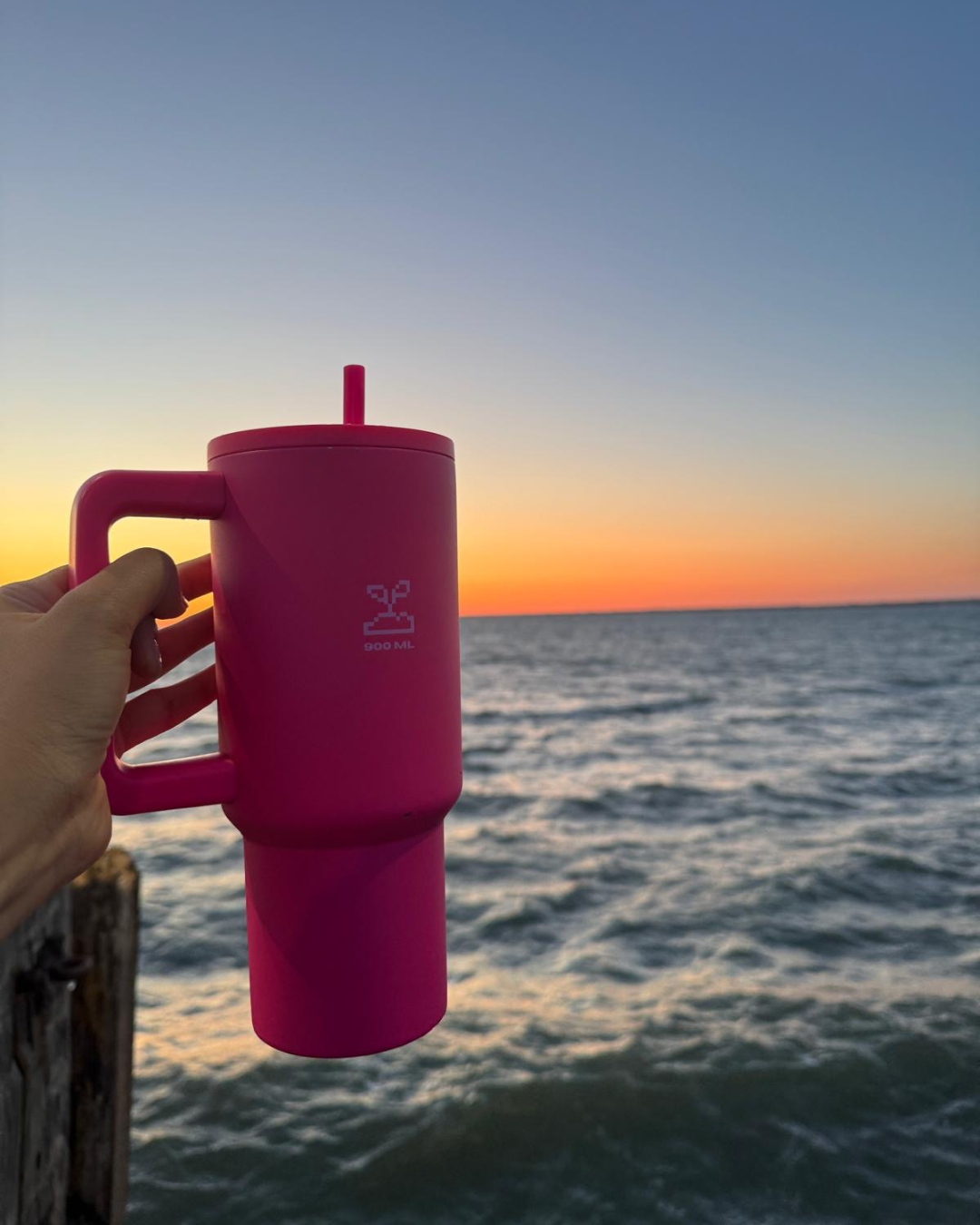 Pink stainless steel bottle held by a hand over a sunset over water stainless steel tumbler 900mL rani pink