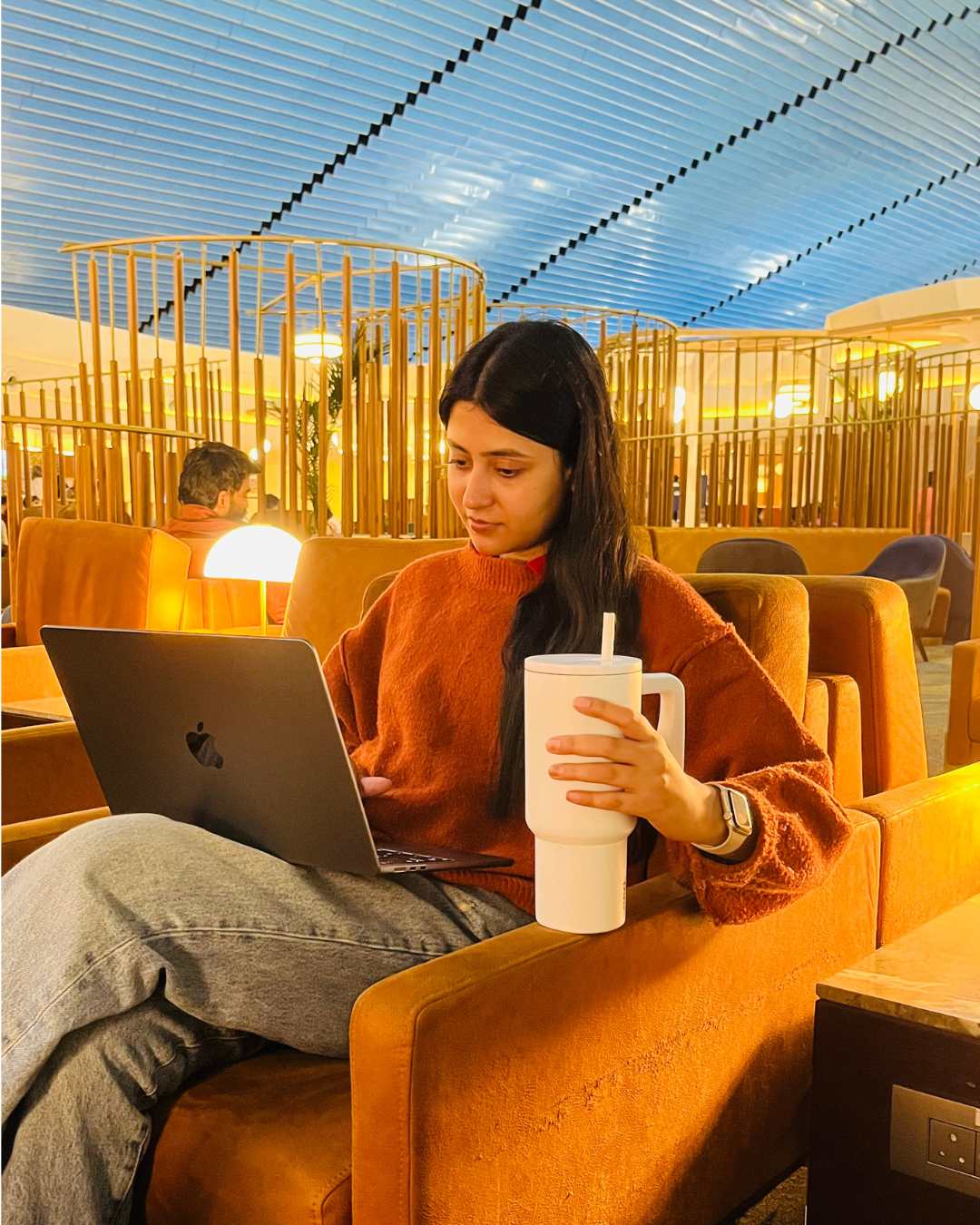 Person sitting on a couch with a laptop and stainless steel stanley cup at an airport lounge stainless steel tumbler 900mL milk tea