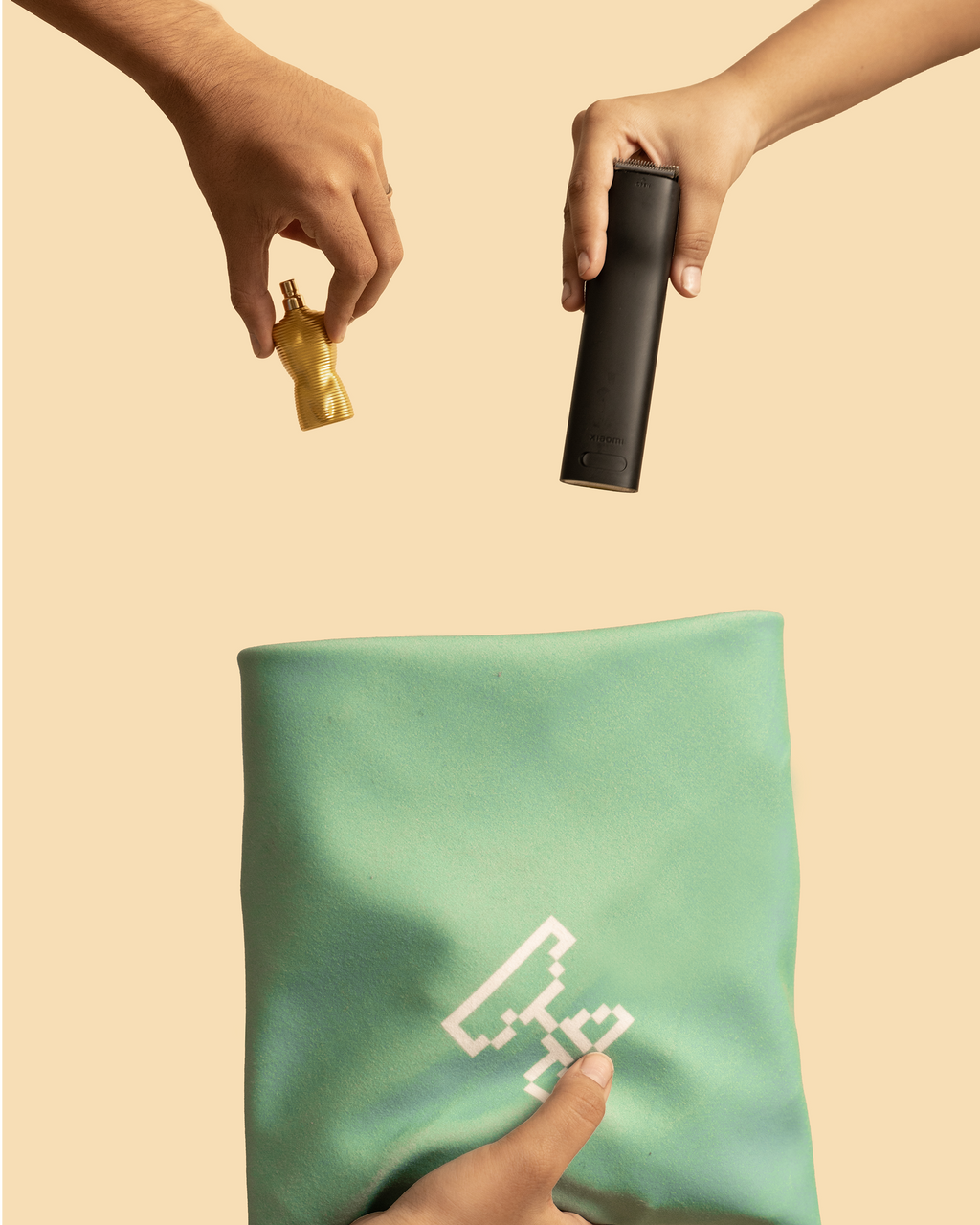 Person holding a black hair trimmer, Jean Paul Gaultier perfume, and green fabric organiser with a logo on a beige background. Hold Up Magic Self Adhesive Wrap Organiser Mint Mojito