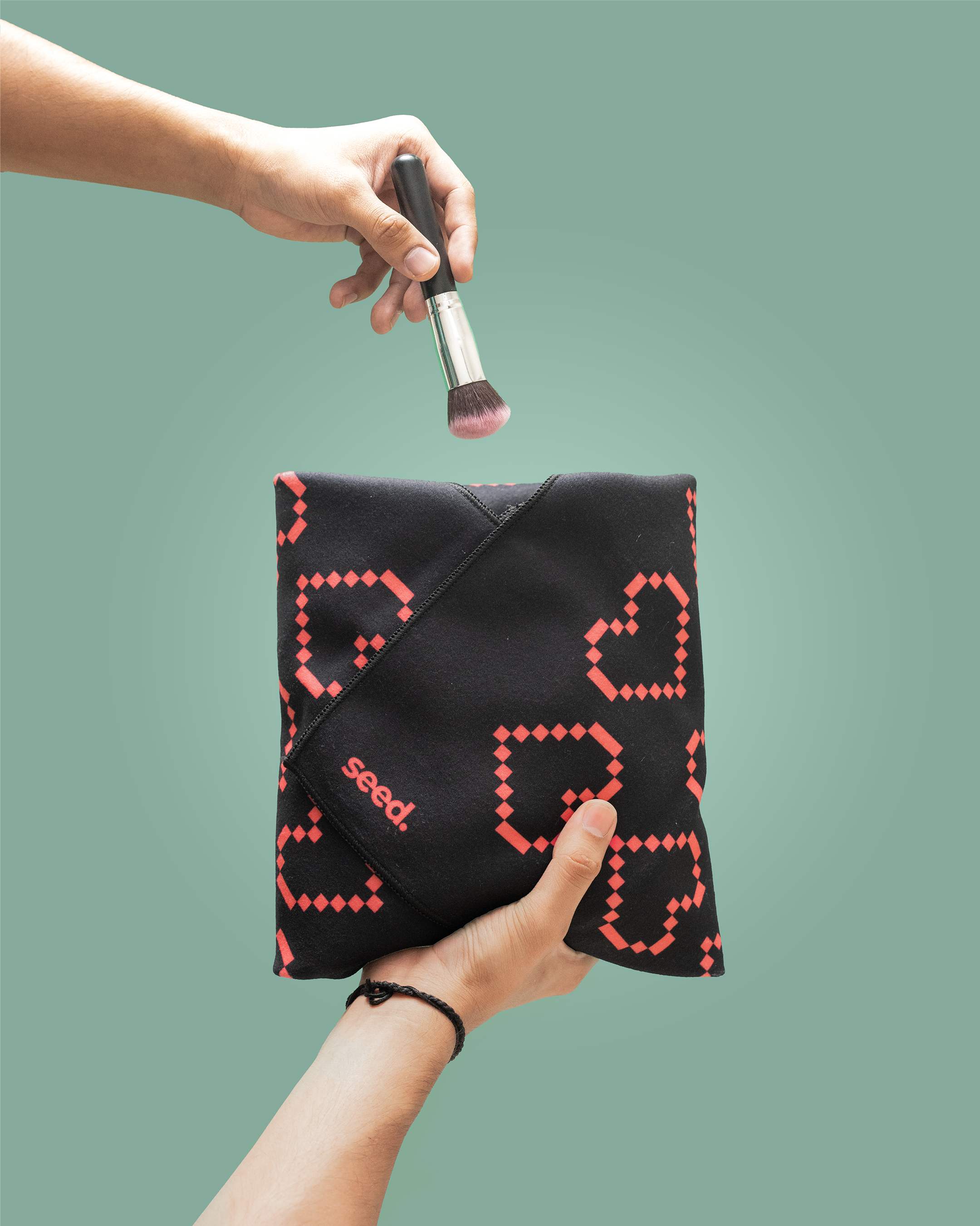 Black makeup pouch with red heart pattern held by a hand, with a brush above it on a green background. Hold Up Magic Self Adhesive Wrap Organiser Tell Tale Heart