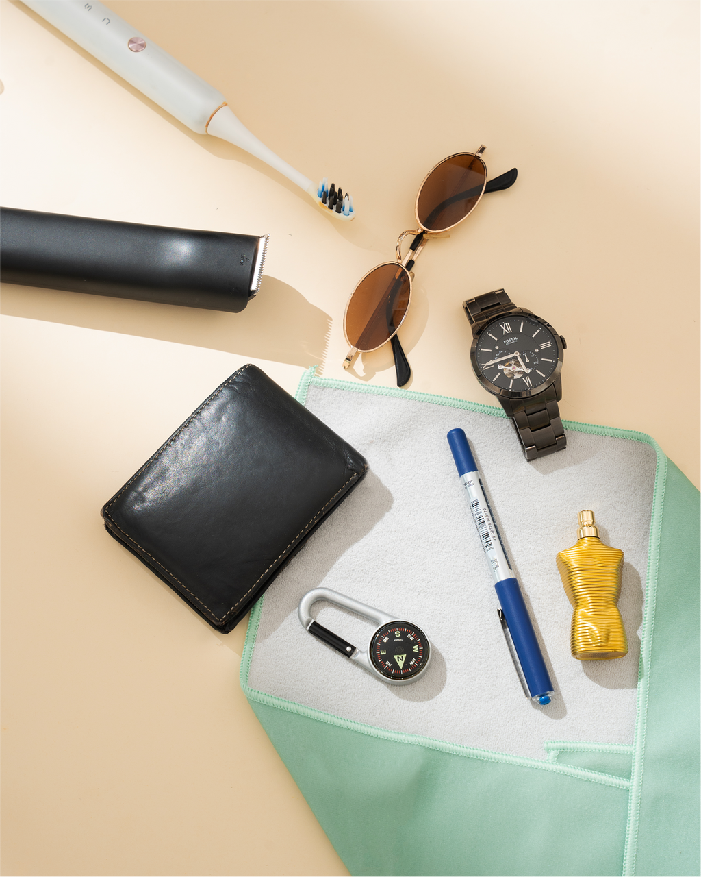 Collection of items including a black wallet, sunglasses, watch, pen, and bottle on a beige surface. Hold Up Magic Self Adhesive Wrap Organiser Mint Mojito
