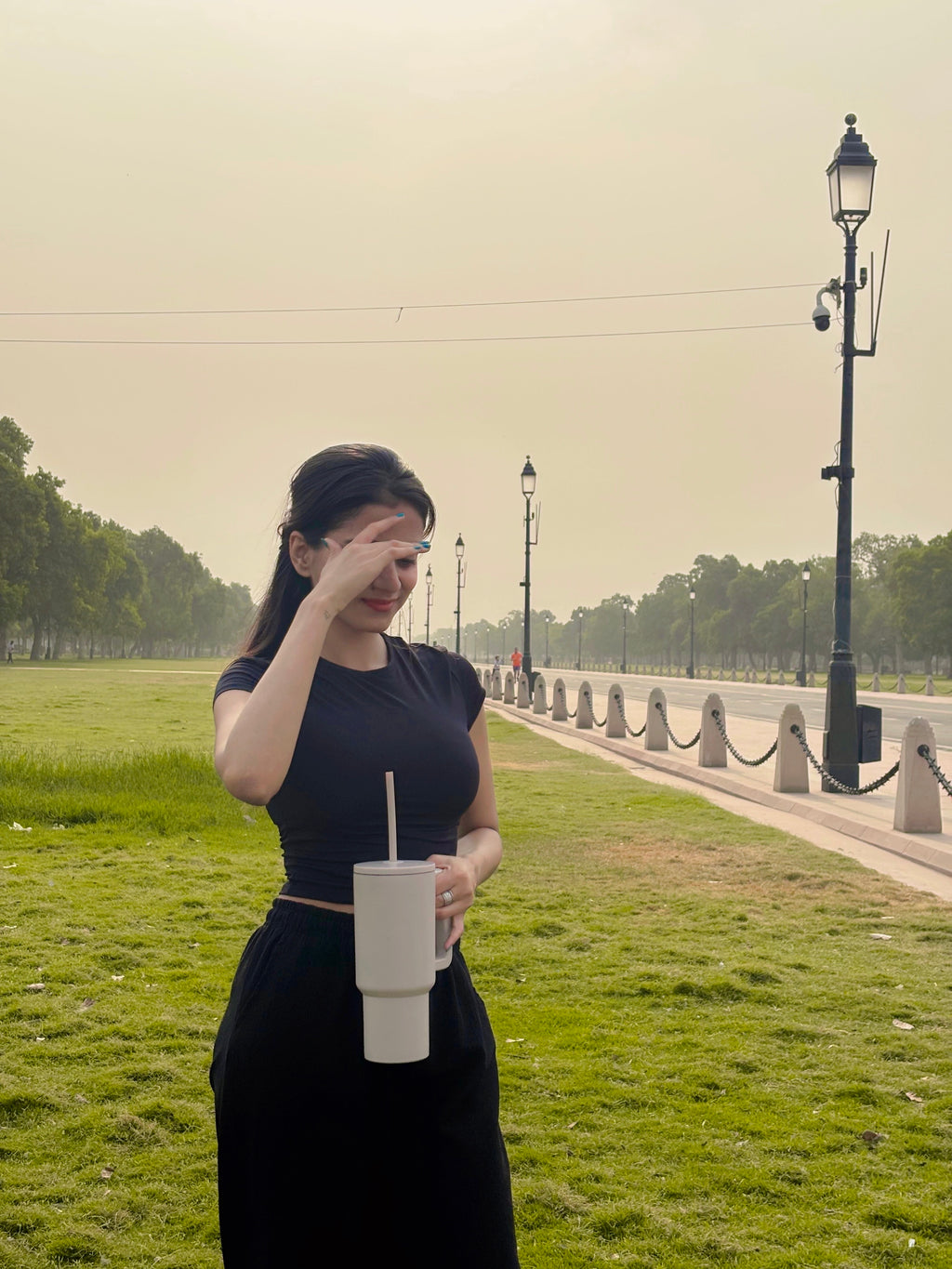 Woman in a park holding a stainless steel tumbler 900mL milk tea, with a road and lamp posts in the background