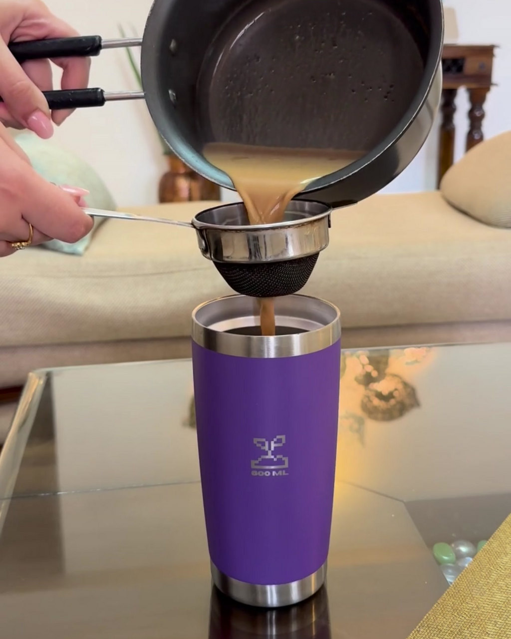 Person pouring chai from a pot into a purple travel coffee mug on a glass table.  insulated stainless steel travel coffee mug 600mL lavender