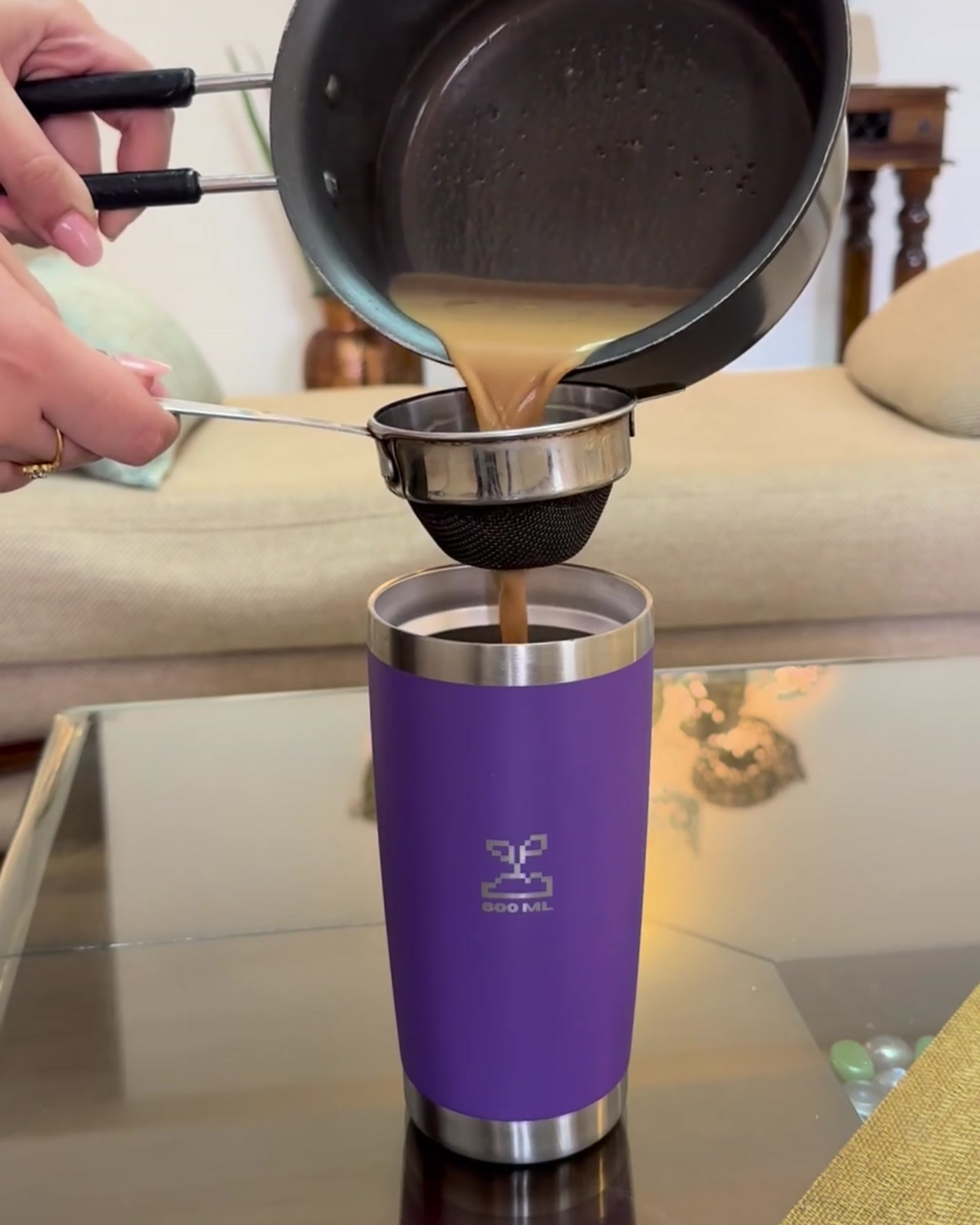 Person pouring chai from a pot into a purple travel coffee mug on a glass table.  insulated stainless steel travel coffee mug 600mL lavender