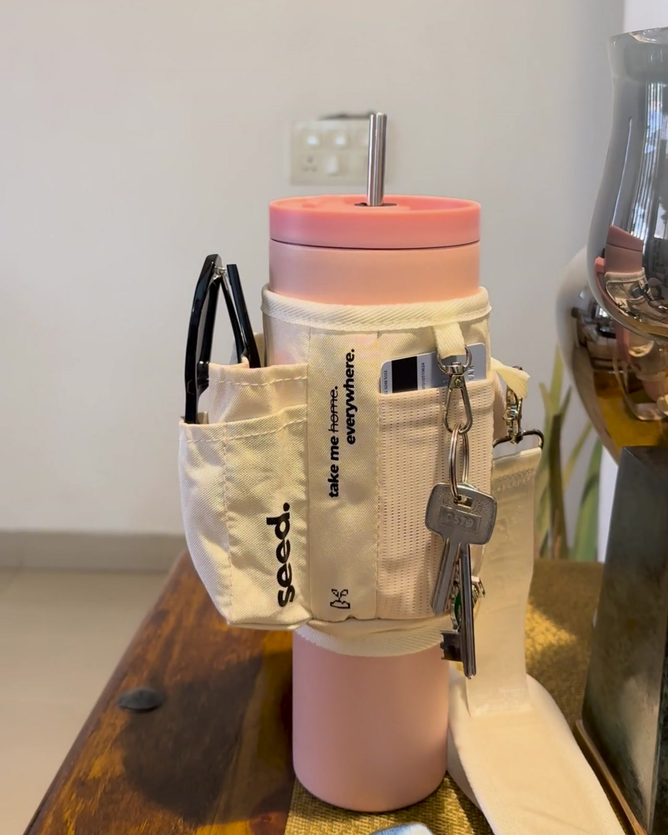 Pink tumbler with a white pouch containing keys and other items on a wooden surface. 1.2l_stainless_steel_tumbler_baby_pink_carry_all_sleeve_white_phone_cards_keys_lip_gloss card cash holder baby pink & milkyway